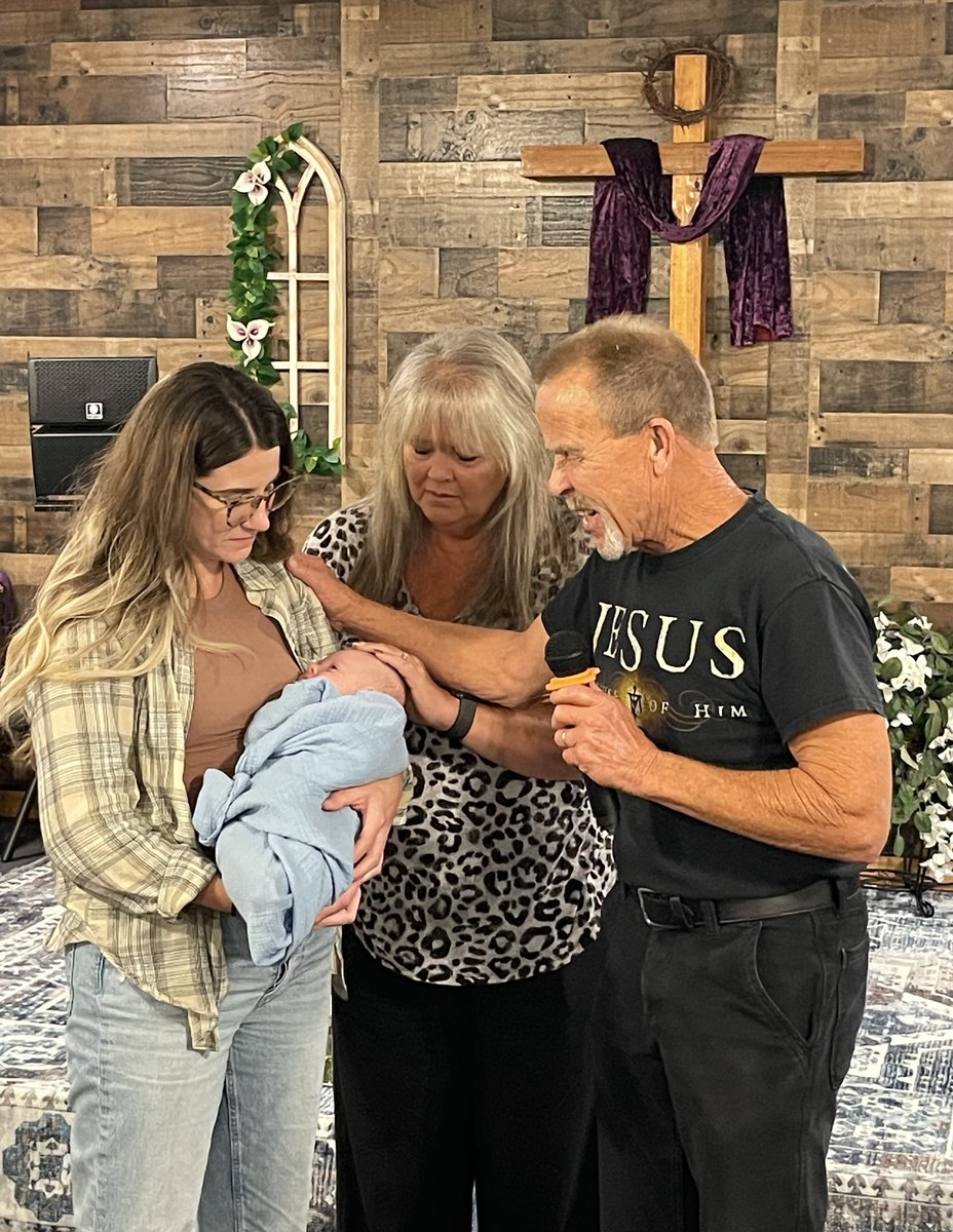 Church family gathered around a baby dedication near a wooden cross