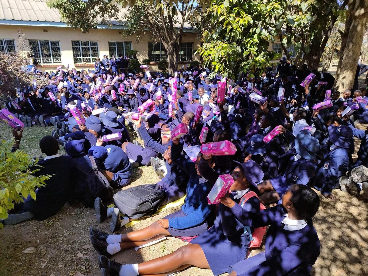 Children in blue and pink uniforms seated together outdoors under trees