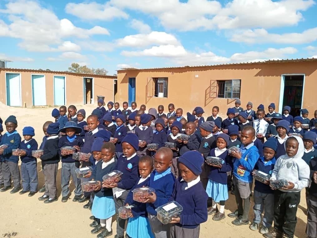 Large group of schoolchildren in blue uniforms gathered outdoors holding gifts from the visit