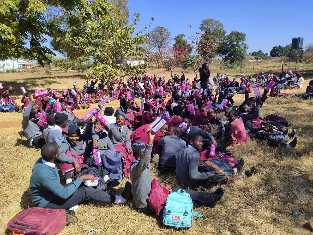 Large group of children seated outdoors with backpacks and supplies